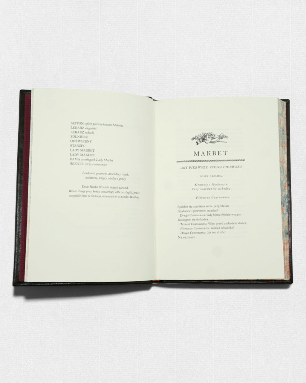 Otwarta książka „Makbet” Williama Shakespeare’a; na prawej stronie początek dramatu (Akt pierwszy, scena pierwsza), na lewej spis postaci, całość w eleganckiej oprawie z marmoryzowanymi krawędziami.