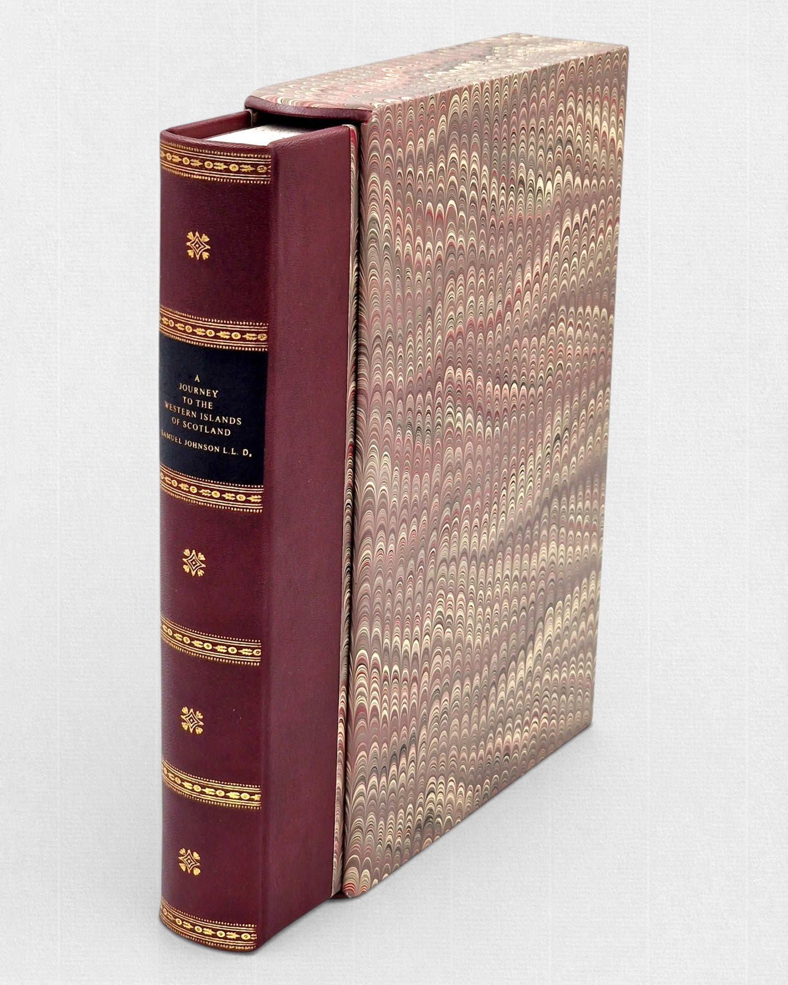 Skórzana, bordowa książka ze złoconym grzbietem i tytułem „A Journey to the Western Islands of Scotland”, częściowo wsunięta w ozdobne etui pokryte papierem marmurkowym w odcieniach brązu i beżu.