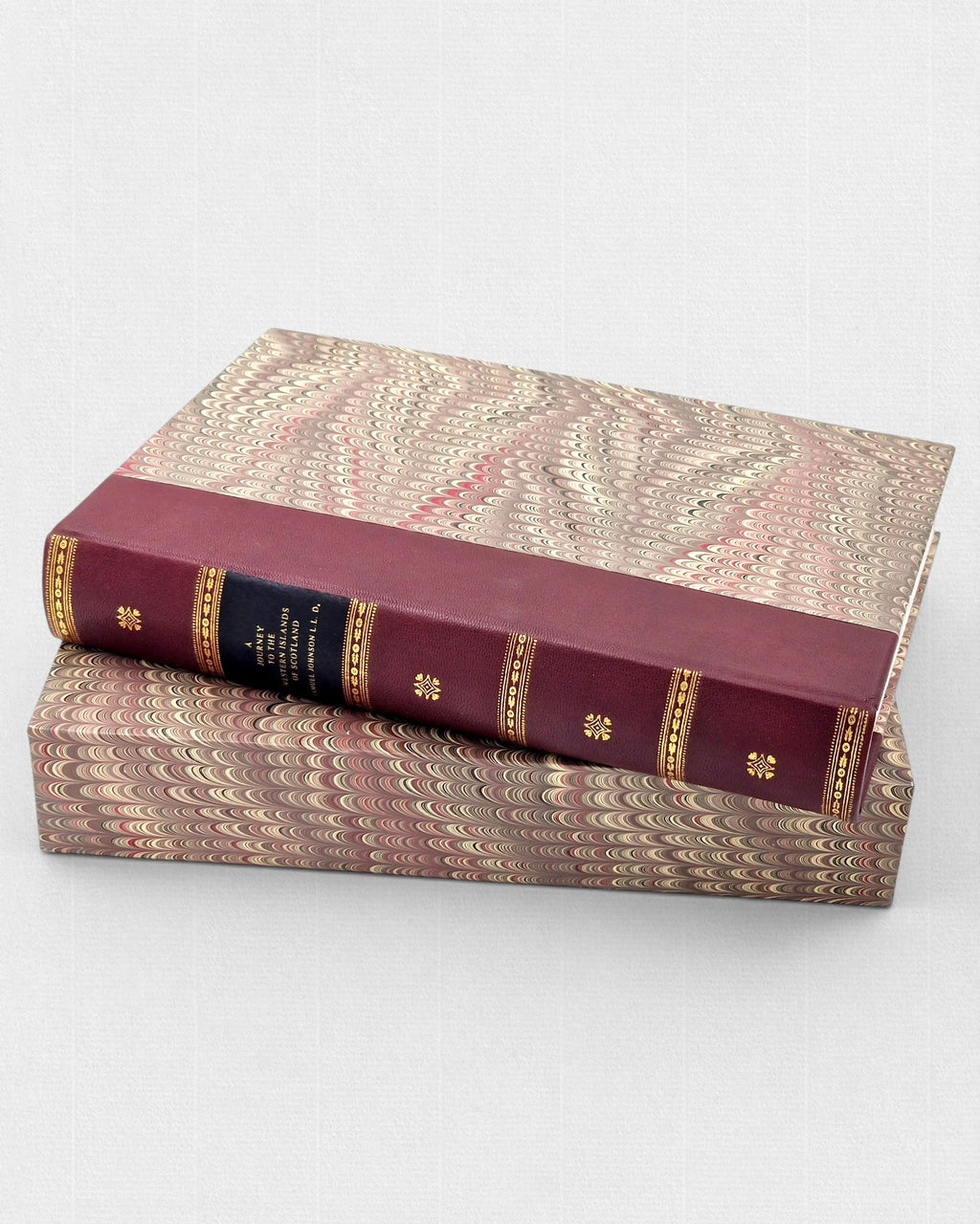 Bordowa, skórzana książka „A Journey to the Western Islands of Scotland” ze złoconymi zdobieniami na grzbiecie, ułożona poziomo na dopasowanym etui pokrytym papierem marmurkowym w odcieniach beżu, brązu i czerwieni.
