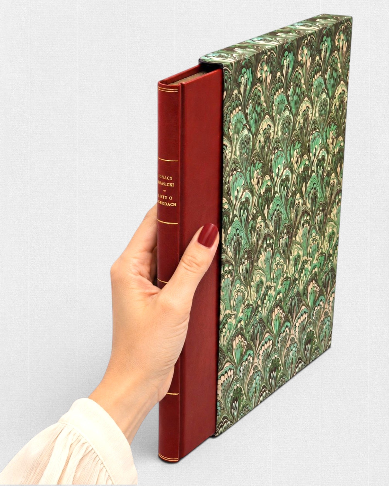 Ignacy Krasicki „Listy o ogrodach” — ręcznie oprawiona książka kolekcjonerska Rambler Press trzymana w kobiecej dłoni, wydanie bibliofilskie w czerwonej skórzanej oprawie z marmoryzowanym etui, inspirowane klasyczną typografią i dawną sztuką książki.