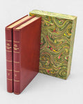 Dwutomowe wydanie „Northanger Abbey” Jane Austen w czerwonej skórzanej oprawie ze złoceniami, obok dekoracyjnego etui w marmurkowy wzór w odcieniach zieleni, żółci i czerwieni.
