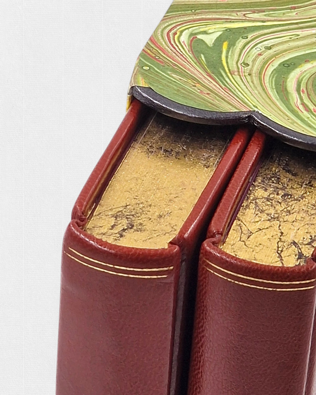 Zbliżenie dwóch tomów „Northanger Abbey” Jane Austen w czerwonej skórzanej oprawie ze złoceniami, z widocznymi złoconymi górnymi krawędziami kart i fragmentem marmurkowego etui.