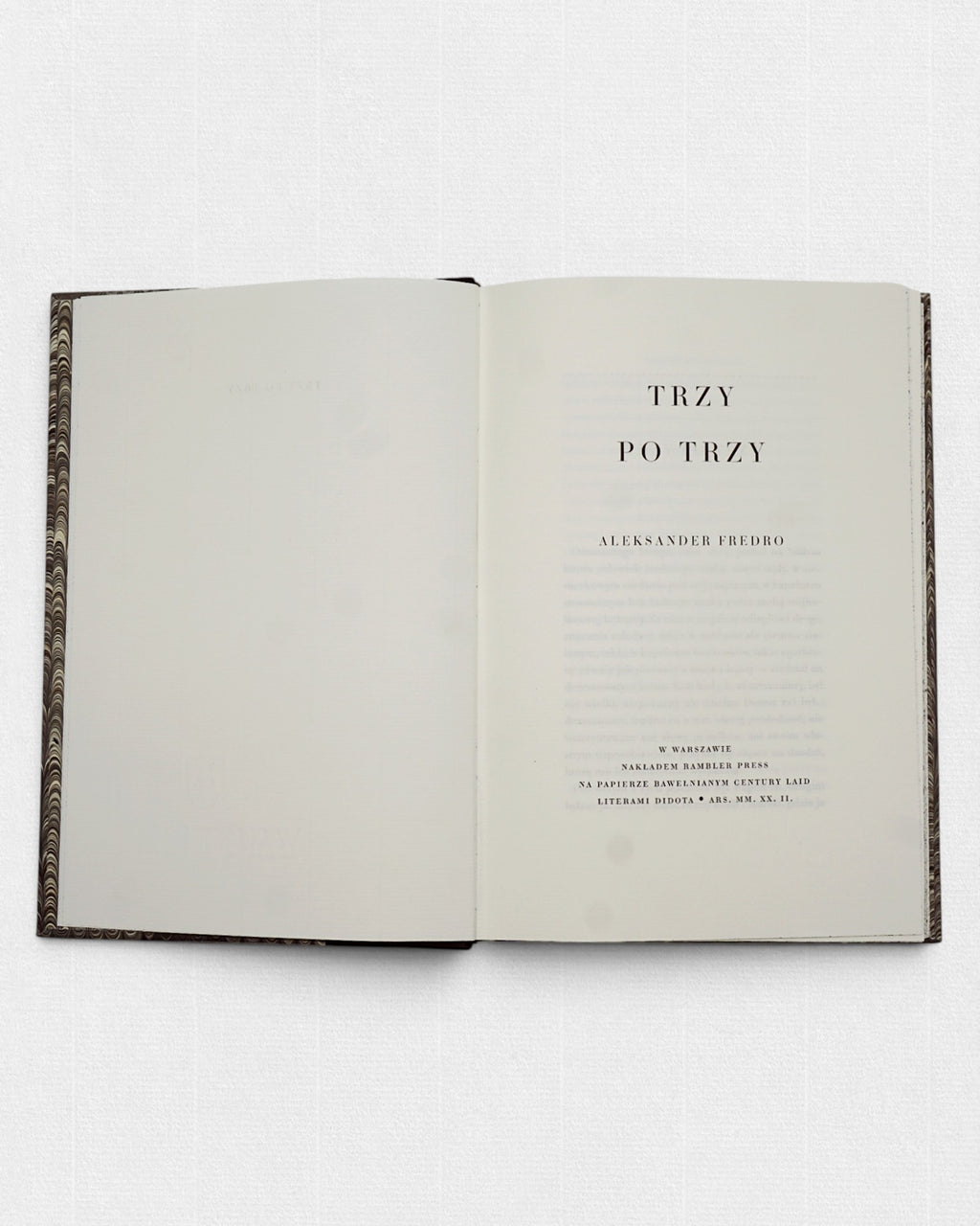 Strona tytułowa kolekcjonerskiego wydania „Trzy po trzy” Aleksandra Fredry przygotowanego przez Rambler Press — klasyczny układ typograficzny inspirowany europejskimi drukami XIX wieku. Książka złożona historycznym krojem pisma Didota i wydrukowana na żeberkowym, bawełnianym papierze Century Laid z filigranem. Widoczne szerokie marginesy, spokojny rytm składu oraz minimalistyczna kompozycja charakterystyczna dla tradycji private press i dawnej sztuki książki. Limitowane wydanie wspomnień Aleksandra Fredry ł