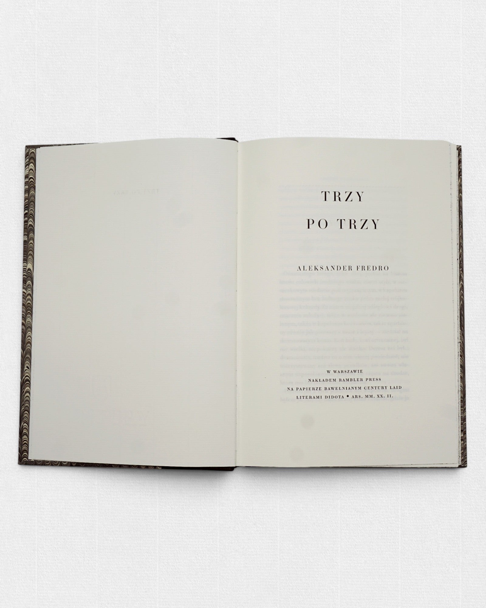 Strona tytułowa kolekcjonerskiego wydania „Trzy po trzy” Aleksandra Fredry przygotowanego przez Rambler Press — klasyczny układ typograficzny inspirowany europejskimi drukami XIX wieku. Książka złożona historycznym krojem pisma Didota i wydrukowana na żeberkowym, bawełnianym papierze Century Laid z filigranem. Widoczne szerokie marginesy, spokojny rytm składu oraz minimalistyczna kompozycja charakterystyczna dla tradycji private press i dawnej sztuki książki. Limitowane wydanie wspomnień Aleksandra Fredry ł