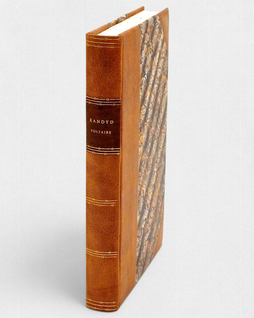 Grzbiet kolekcjonerskiego wydania „Kandyda” Woltera w ręcznej oprawie skórzanej z tłoczeniami i dekoracyjnym papierem marmurkowym — edycja bibliofilska Rambler Press.